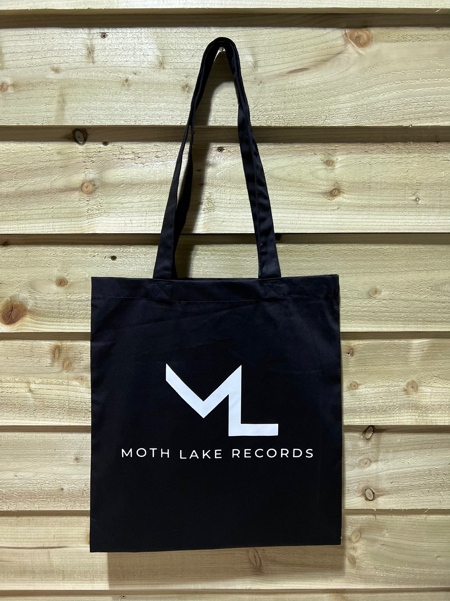 Black tote bag with Moth Lake Records logo on a wooden background