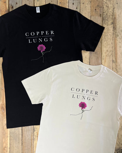 Black and white t-shirts with 'Copper Lungs' flower design on a wooden surface